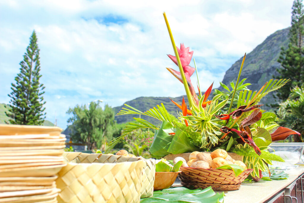 Food in baskets on a table surrounded by tropical scenery, at one of the best Hawaii activities, a Hawaiian luau