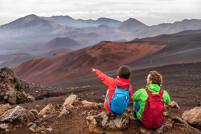 A couple in rain jackets sits on the edge of the Haleakala crater on Maui, Hawaii. 