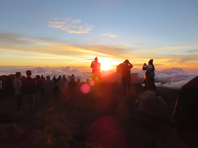 People gather at Haleakala National Park as the sun rises over the crater.