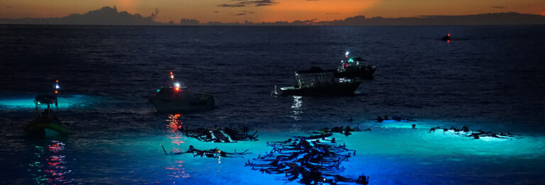Snorkelers gather around underwater lights in the ocean at night on the Manta Ray Snorkel Kona.