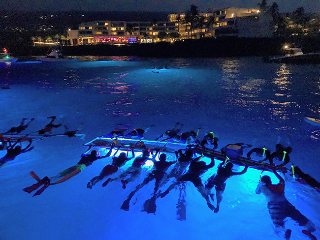 Snorkelers hang on to floating lights at night, near the shore in Kona Hawaii