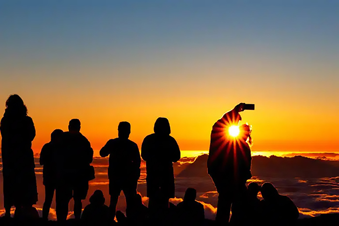A group watches the sunset from high on a mountain, above the clouds. 