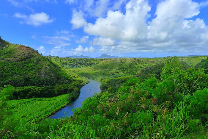 Boats cruise up the Wailua River in a lush green valley with mountains in the background.