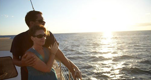 Two guests stand on the deck of a catamaran, watching a Hawaiian sunset.